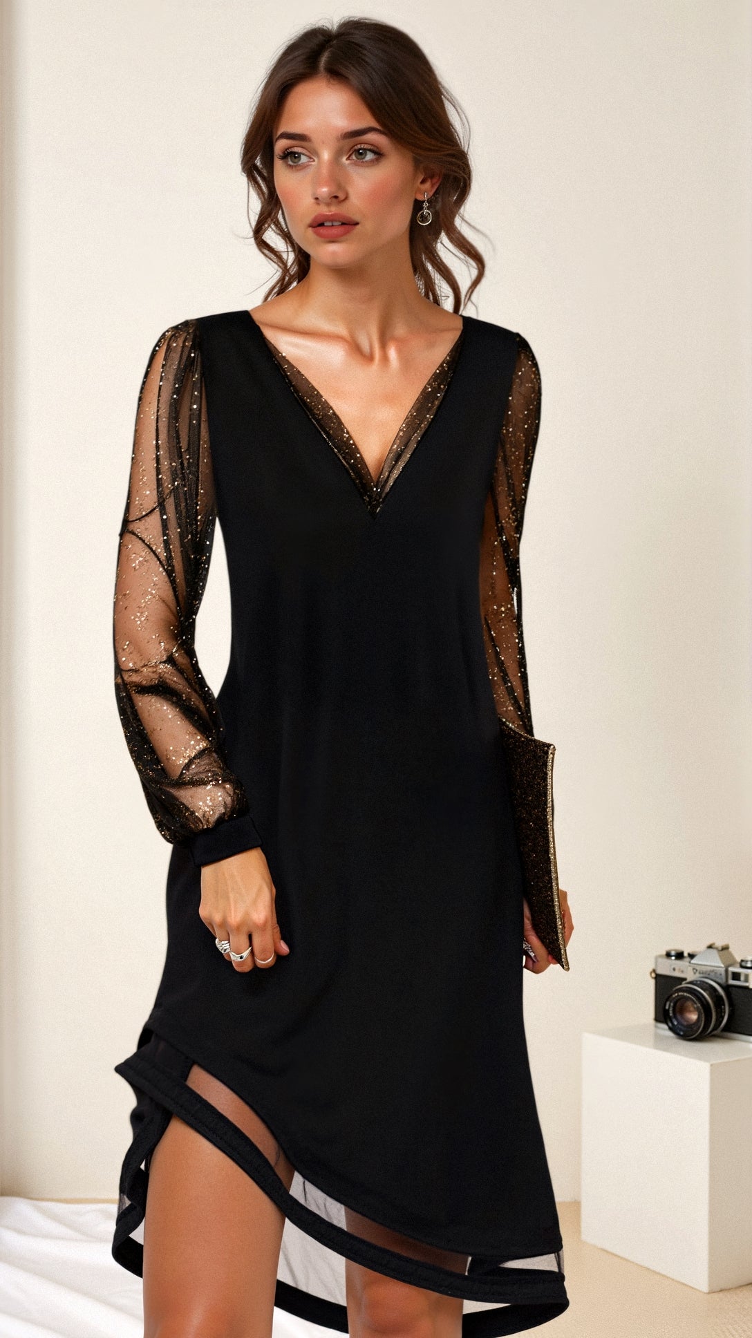 Elegante zwarte feestjurk met een v-hals en lange, doorschijnende mouwen met subtiele glitters. De jurk heeft een speelse split aan de zijkant en een klassieke, verfijnde uitstraling. Perfect voor een glamoureuze avond, combineer het met een clutch voor een chique look. De glinsterende details maken deze jurk ideaal voor elke speciale gelegenheid.