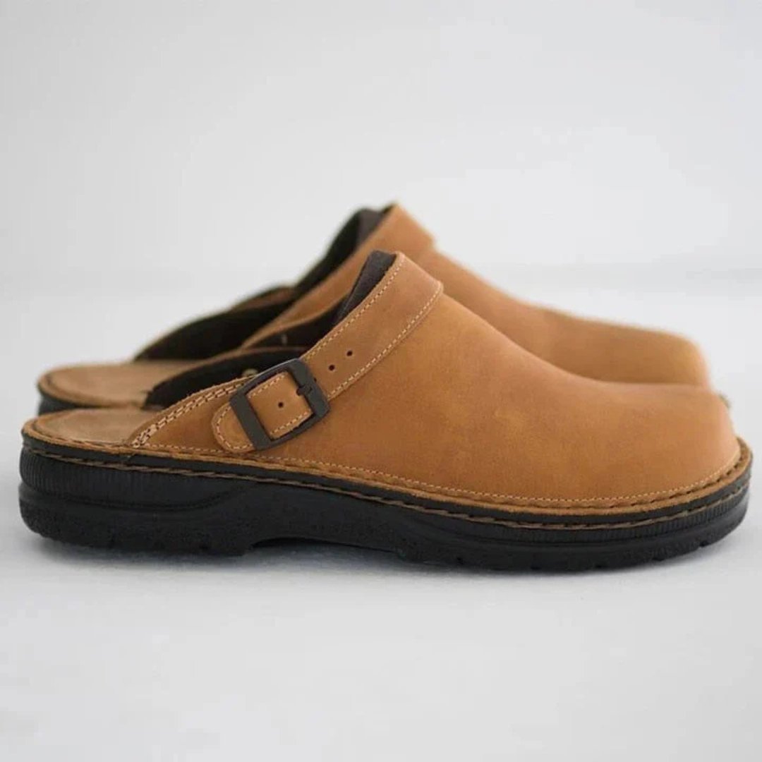 Afbeelding van de Urbano loafers in een warme camel-kleur leren uitvoering. Deze comfortabele instappers hebben een open hielontwerp en een verstelbare gesp voor een persoonlijke pasvorm. De stevige zwarte zool biedt uitstekende grip en ondersteuning, terwijl het zachte voetbed zorgt voor ultiem draagcomfort. Perfect voor zowel binnen- als buitengebruik, met een klassieke en tijdloze uitstraling.