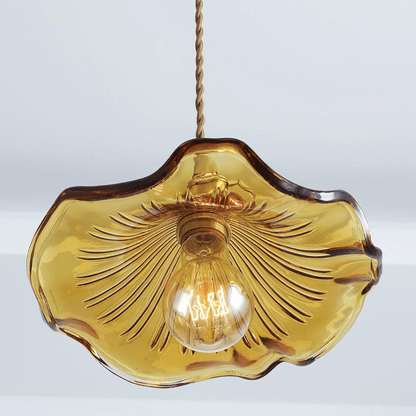 Close-up van de BloomLume hanglamp met een golvende amberkleurige glazen kap en een elegante gouden fitting. De warme gloed van het filamentlampje benadrukt het unieke ontwerp, ideaal voor het toevoegen van een stijlvolle en natuurlijke sfeer aan woonkamers, eetruimtes of creatieve interieurs.
