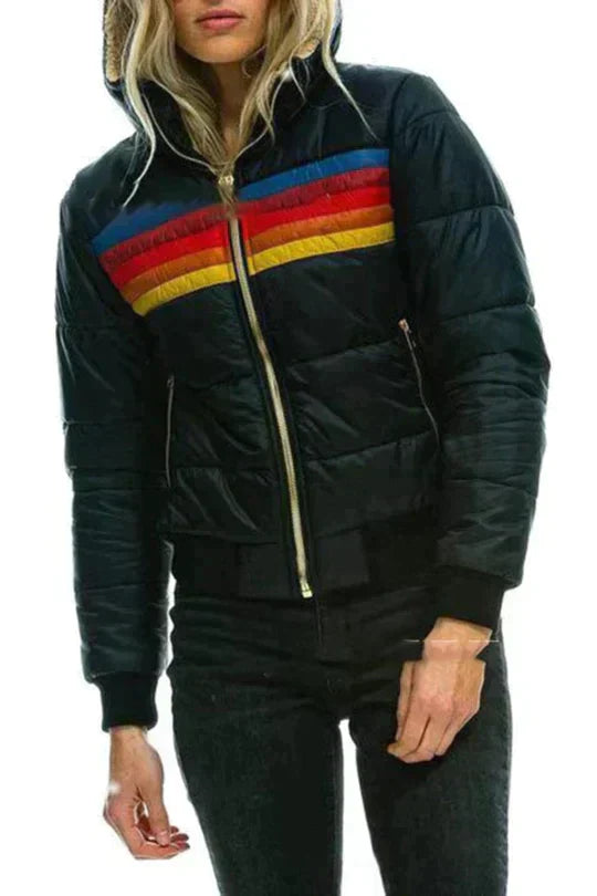 De afbeelding toont een vrouw die een gewatteerde, zwart gekleurde jas draagt met een sportieve en retro uitstraling. De jas heeft kleurrijke horizontale strepen in rood, geel en blauw op de borst en schouders, en is voorzien van een rits aan de voorkant en een elastische boordenafwerking. De jas heeft een comfortabele pasvorm en biedt zowel stijl als functionaliteit, ideaal voor een casual en elegante look tijdens de koudere maanden.