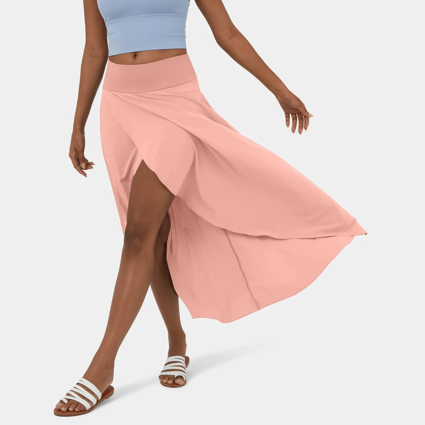 Een vrouw draagt een elegante donkerblauwe rok die sierlijk meebeweegt terwijl ze loopt. De rok heeft een vloeiende snit met een hoge taille en is gecombineerd met een lichtblauw sporttopje en witte sandalen, perfect voor een stijlvolle en comfortabele zomerse look.