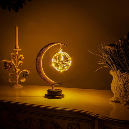 Een prachtige maanlamp met een gloeiende bol van licht, die een magische sfeer uitstraalt. De lamp staat op een zwarte basis en heeft delicate draadlampjes die een warme en betoverende ambiance creëren, perfect voor interieurdecoratie.