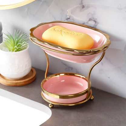 GleamEdge zeepbakje in zachtroze met gouden accenten, geplaatst op een elegante tweelaagse metalen standaard. Dit moderne en praktische ontwerp houdt zeep droog en voegt een luxe uitstraling toe aan elke badkamer.