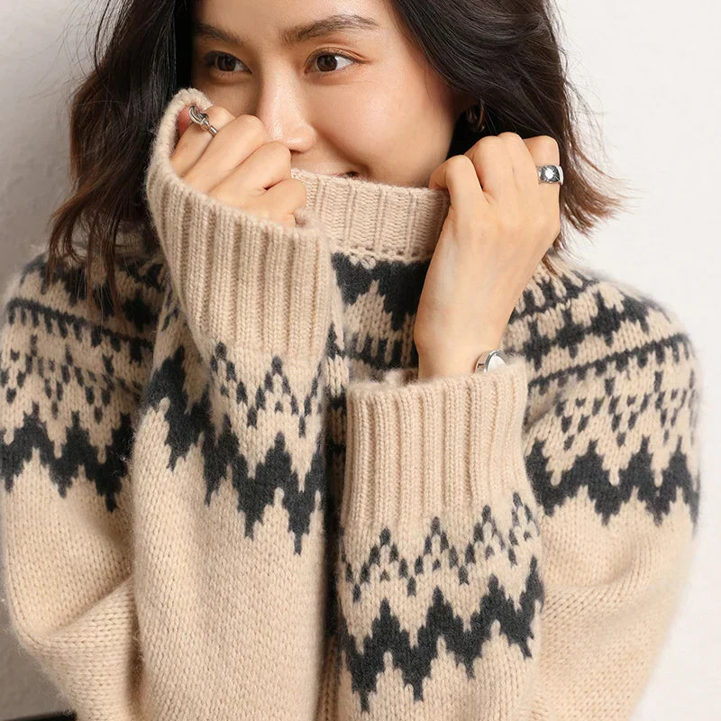 GloVibe trui in beige met een modern zwart geometrisch patroon. De trui heeft een hoge col en lange mouwen met brede boorden voor extra comfort. Perfect voor een stijlvolle en warme uitstraling in de koude maanden.