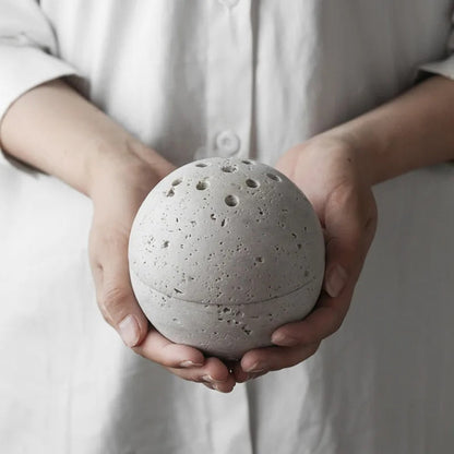 Grazia wierookhouder met rustgevend ontwerp, vastgehouden door een persoon in witte kleding. De ronde, stenen houder heeft meerdere gaten voor wierookstokjes en straalt eenvoud en sereniteit uit. Perfect voor ontspanning en meditatie in elke ruimte.