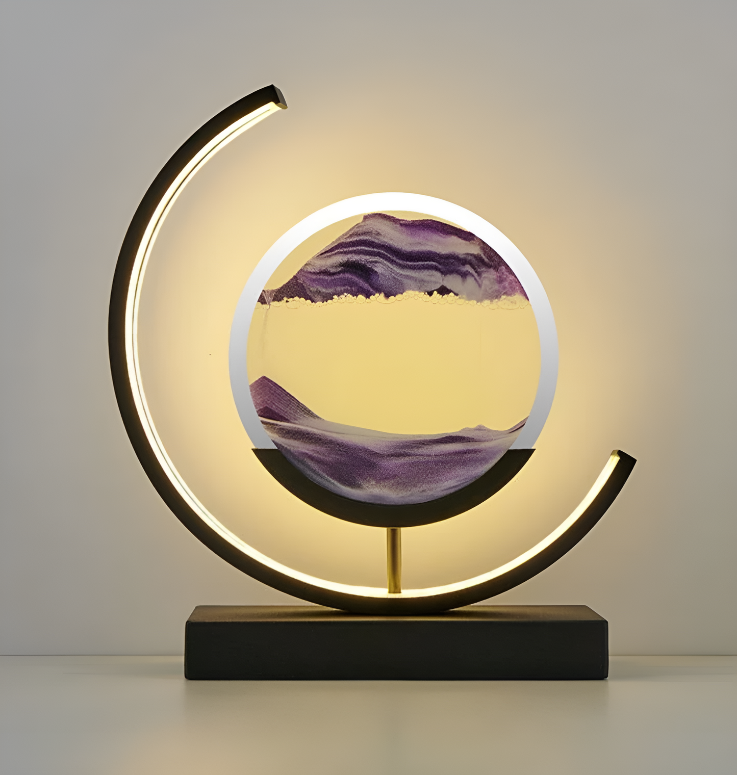 De afbeelding toont een elegante LED-lamp met een uniek zandkunstontwerp. Het zand, in verschillende tinten paars, vormt een prachtig landschap met golvende bergen en een zacht gekleurde lucht. De lamp is omlijst door een gebogen LED-licht, dat een warme gloed uitstraalt en de zandkunst prachtig verlicht. De lamp staat op een stijlvolle zwarte basis, wat het moderne en verfijnde ontwerp complementeert. Deze lamp is een perfecte aanvulling voor een sfeervol en stijlvol interieur.