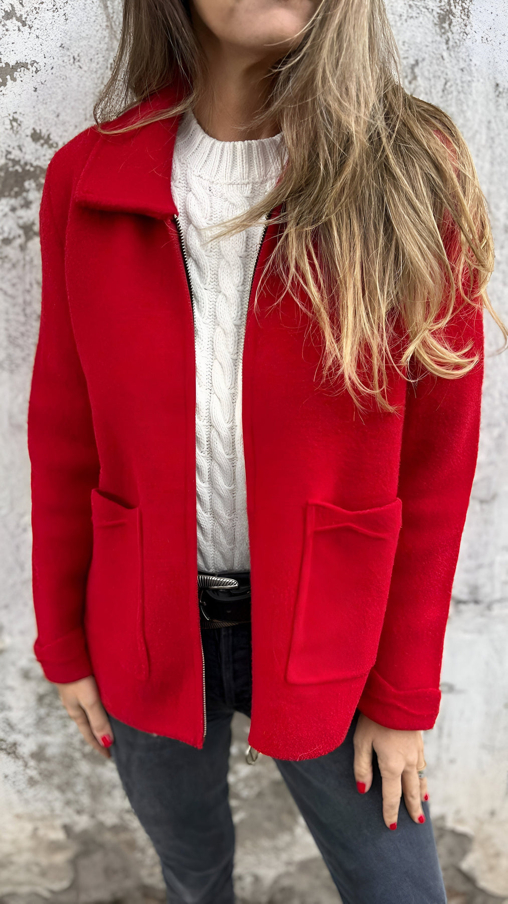 Kallia damesjas in felrood, gedragen over een witte kabeltrui. De jas heeft een moderne pasvorm met grote voorzakken en een ritssluiting. Perfect voor een stijlvolle en comfortabele look tijdens koudere dagen.