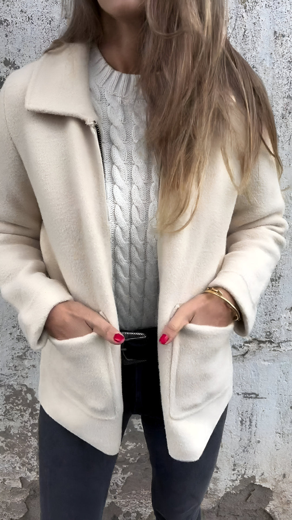 Kallia damesjas in crèmewit, gedragen over een witte kabeltrui. De jas heeft een tijdloos ontwerp met praktische zakken en een comfortabele pasvorm. Ideaal voor een elegante en warme uitstraling tijdens de winter.