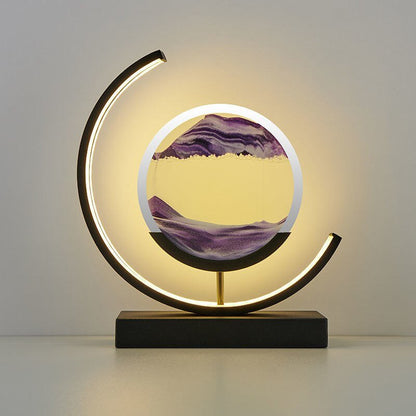 De LumiAura lamp creëert een magische sfeer met een prachtig zandlandschap dat in beweging blijft. Het minimalistische, cirkelvormige ontwerp, verlicht door een zachte rand, benadrukt de hypnotiserende zandstroom in een levendig paars. Deze lamp is niet alleen een lichtbron, maar ook een dynamisch kunstwerk dat rust en elegantie toevoegt aan elk interieur. Perfect voor moderne woonruimtes waar sfeer en stijl centraal staan.