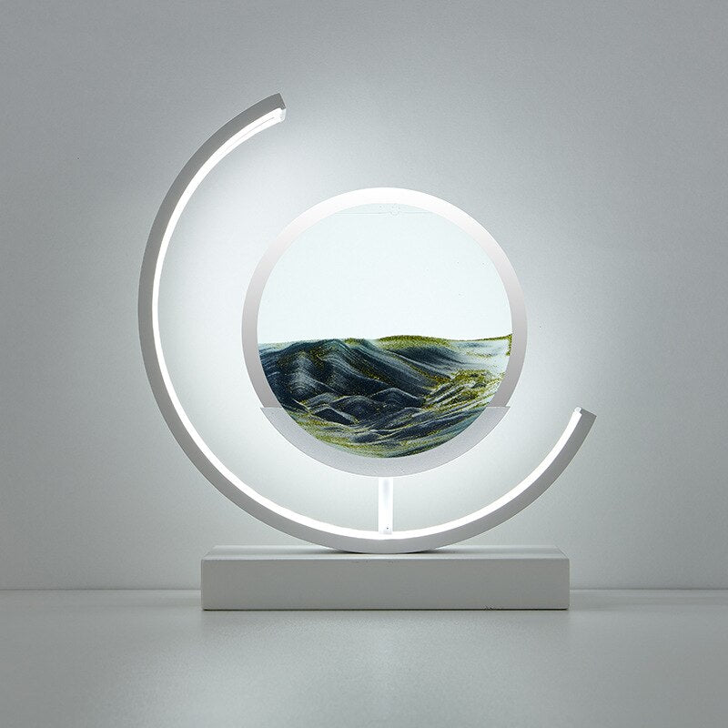 De LumiAura lamp toont een rustgevend zandlandschap in zachte groene tinten, met de zandlagen die langzaam bewegen, verlicht door het omringende zachte licht. Het strakke, moderne ontwerp voegt een kalmerende sfeer toe aan elke kamer, perfect voor ontspanning. Het kunstzinnige zandlandschap creëert een betoverende uitstraling, waardoor het een perfecte aanvulling is voor je interieur.