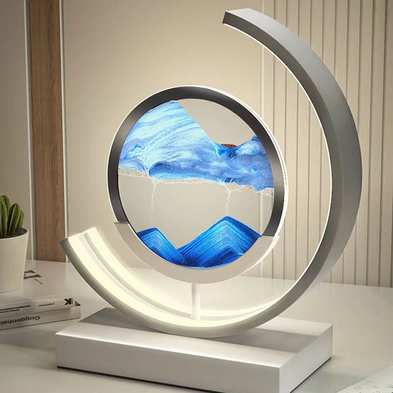 De LumiAura lamp is een adembenemend kunstwerk dat verlichting combineert met een hypnotiserend zandlanschap. Het minimalistische ontwerp in een cirkelvormige setting geeft een modern en rustgevend effect, terwijl de zandstroom langzaam verandert van patroon en kleur, waardoor het een dynamisch visueel effect biedt. Perfect voor elk interieur waar je stijl en kalmte wilt toevoegen.