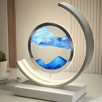 De LumiAura lamp is een adembenemend kunstwerk dat verlichting combineert met een hypnotiserend zandlanschap. Het minimalistische ontwerp in een cirkelvormige setting geeft een modern en rustgevend effect, terwijl de zandstroom langzaam verandert van patroon en kleur, waardoor het een dynamisch visueel effect biedt. Perfect voor elk interieur waar je stijl en kalmte wilt toevoegen.