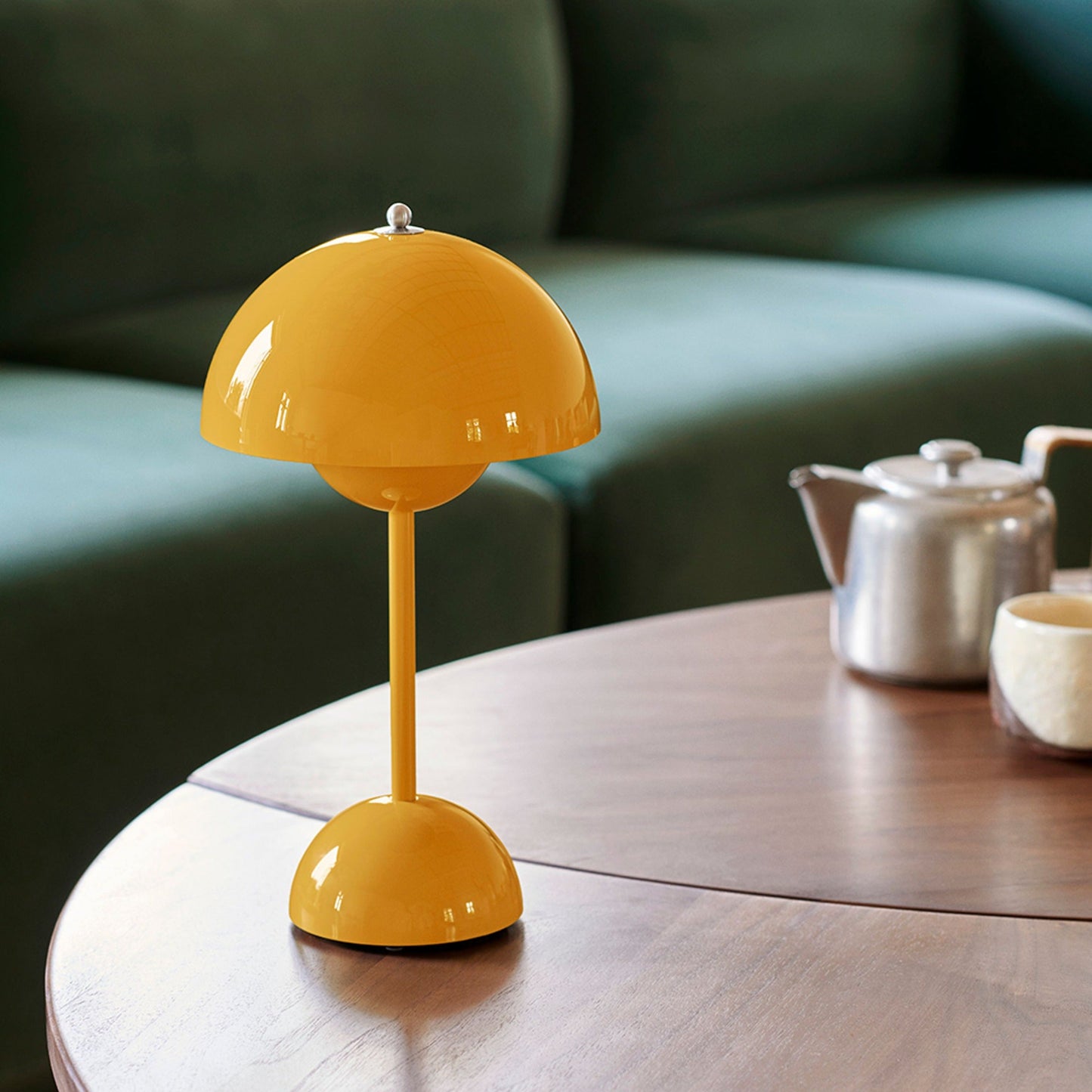 Geelgekleurde LumiNova LED-tafellamp op een houten salontafel, geplaatst in een moderne woonkamer met een groene bank, biedt een stijlvolle en warme verlichting.