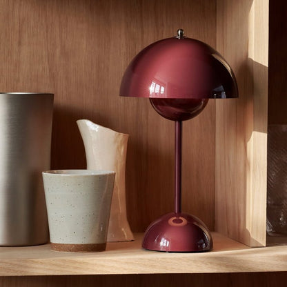 Dieprode LumiNova LED-tafellamp elegant gepresenteerd op een houten plank, gecombineerd met keramische en metalen decoratieve accessoires, creëert een warme en stijlvolle sfeer.