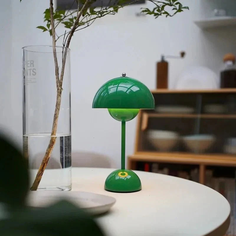 Een speelse LumiNova tafellamp in groen, met een unieke bloemvormige basis, geplaatst op een moderne ronde tafel. De lamp straalt een zachte, warme gloed uit en voegt een frisse, stijlvolle uitstraling toe aan elke ruimte, ideaal voor een sfeervolle inrichting.