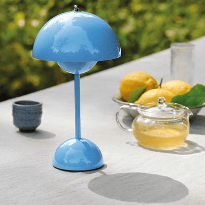 Helderblauwe LumiNova LED-tafellamp elegant geplaatst op een buiten tafel, naast een glazen theepot en verse citroenen, perfect voor stijlvolle buitenverlichting.