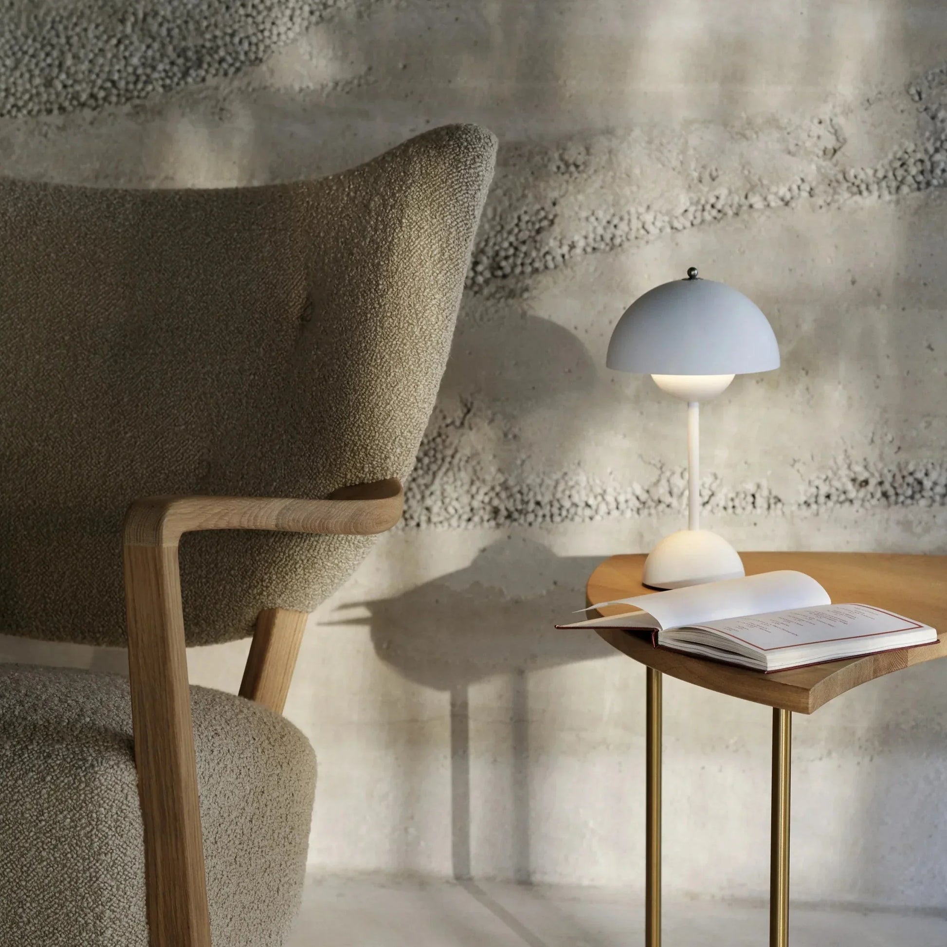 Elegante LumiNova LED-tafellamp in wit, geplaatst op een houten bijzettafel met een open notitieboek, naast een moderne fauteuil in een minimalistisch interieur.