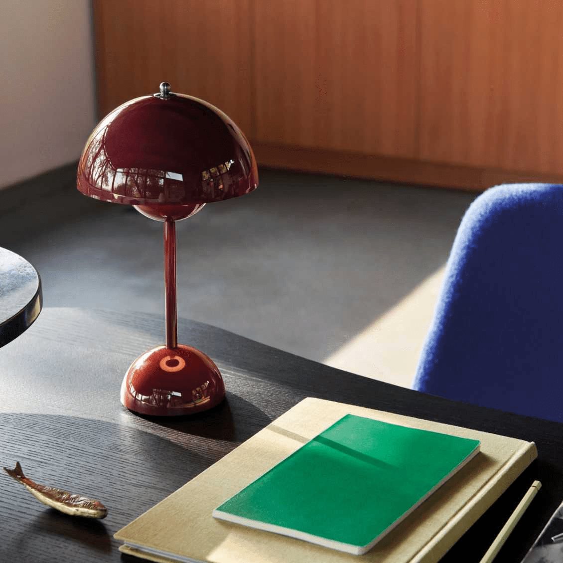 De LumiNova LED-tafellamp in een diepe bordeauxrode kleur, elegant geplaatst op een modern bureau met een groene notitieboek en gouden accessoires, ideaal voor een stijlvolle werkruimte.
