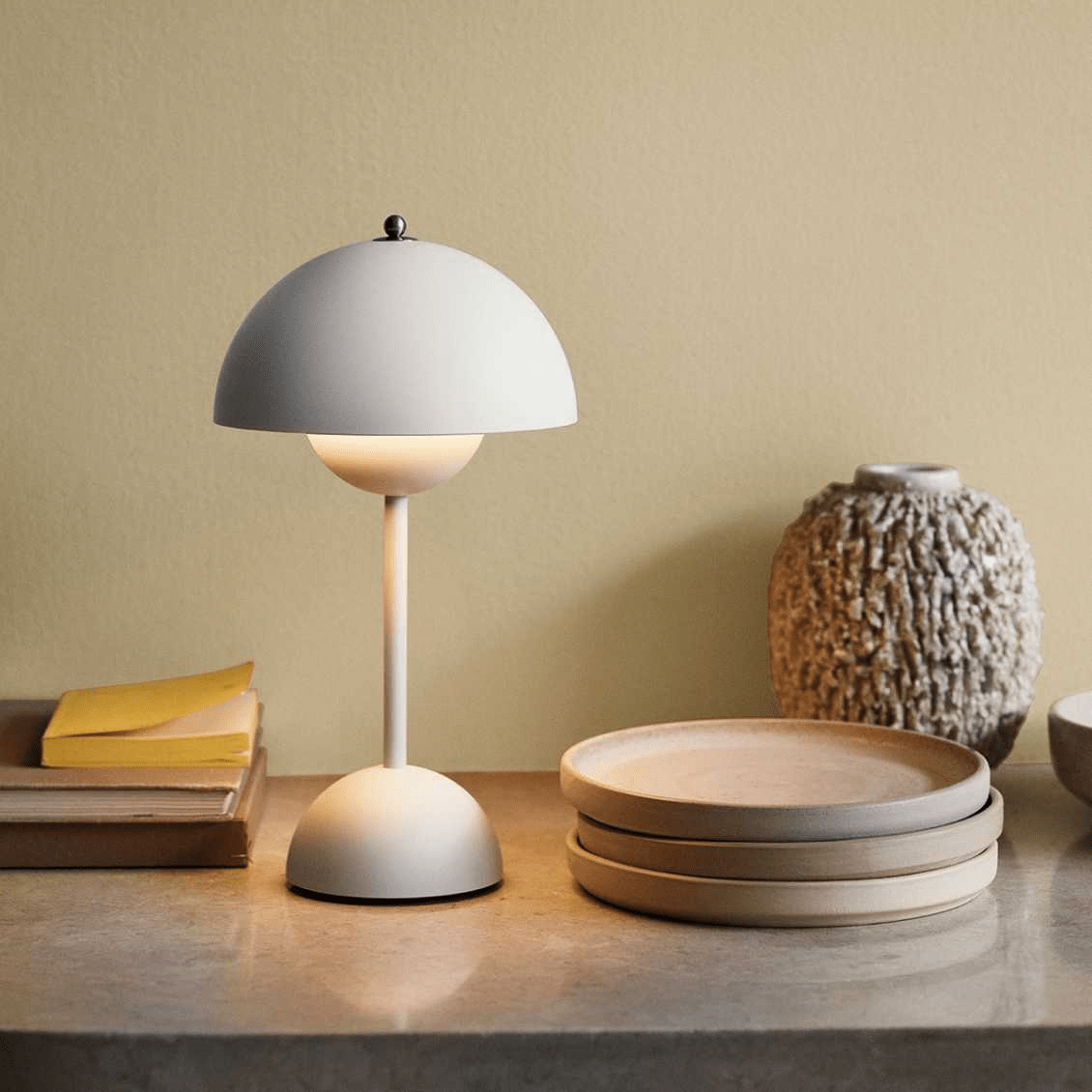 De LumiNova LED-tafellamp in een zachte crèmekleur, sfeervol geplaatst op een natuurstenen oppervlak, omringd door minimalistische decoraties voor een warme en moderne ambiance.