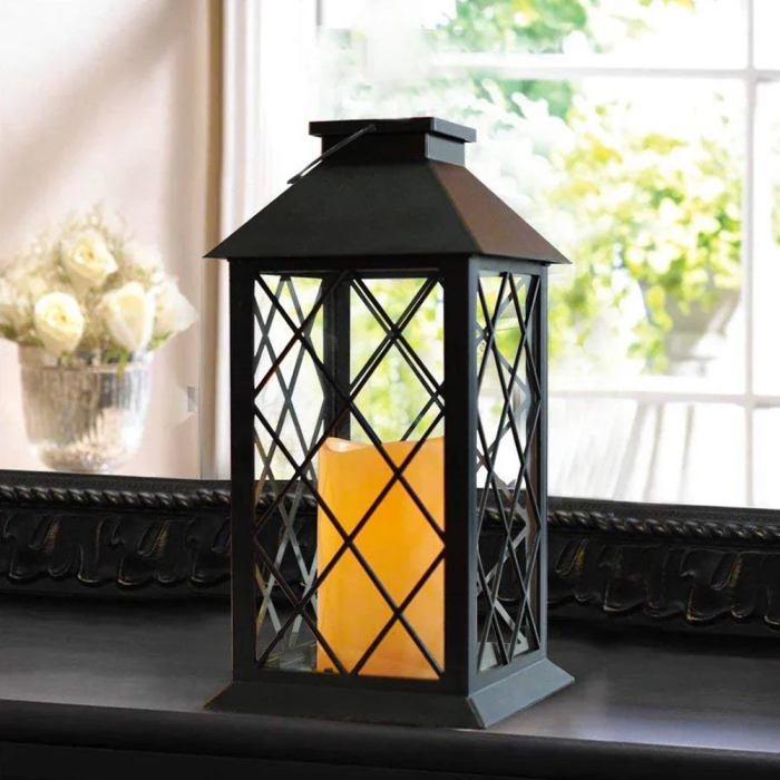 Zwarte lantaarn met een geometrisch ontwerp, verlicht door een vlamvrije gele kaars, geplaatst op een donkere houten tafel. De lantaarn straalt een rustige en gezellige sfeer uit, ideaal voor het creëren van een ontspannen ambiance in huis.