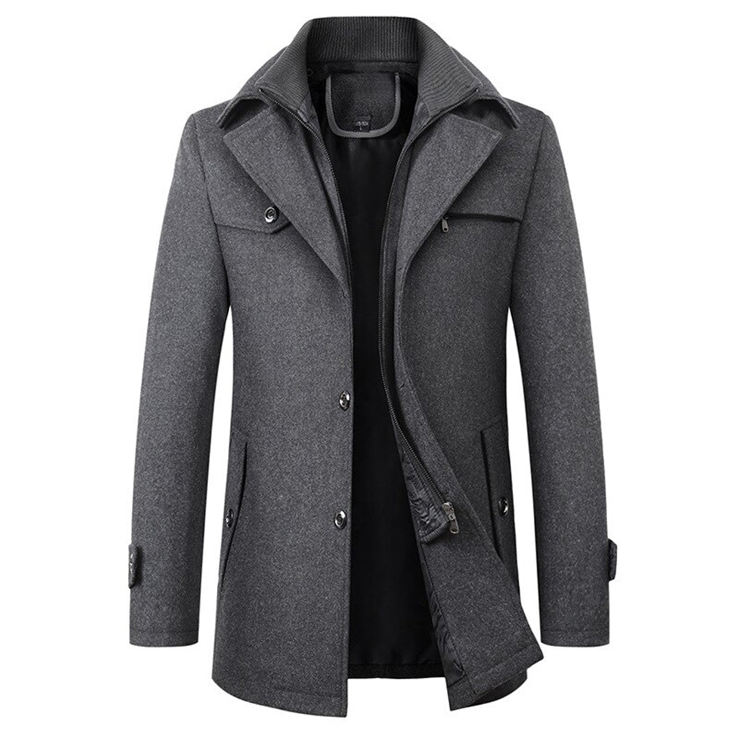 Een chique, grijze winterjas met een moderne, slanke snit. De jas beschikt over een dubbele sluiting met knopen en een ritssluiting voor extra bescherming tegen de kou. De opstaande kraag en de zakken aan de zijkanten bieden zowel stijl als functionaliteit, terwijl de comfortabele binnenvoering de warmte vasthoudt. Perfect voor een luxe winterlook.