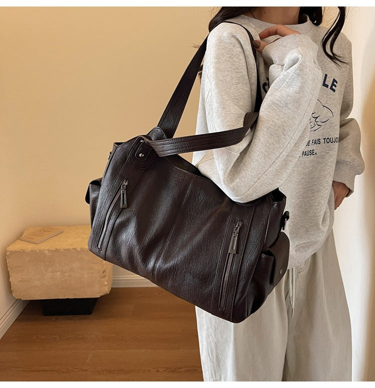 OLYNDA bruine tote tas gedragen over de schouder, met ritsvakken aan de voorkant en een praktische schouderriem, perfect voor dagelijks gebruik.