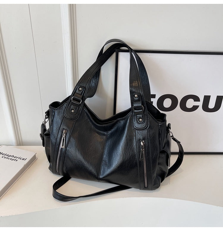 OLYNDA zwarte leren tote tas met ritsvakken, stijlvol neergezet op een tafel naast een 'focus' poster, praktisch en tijdloos ontwerp.