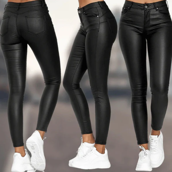 Een vrouw draagt een elegante, zwarte, hoog-taille broek van Onyx met een strakke pasvorm en een subtiele glans. De broek heeft een moderne uitstraling en is gecombineerd met witte sneakers voor een casual en stijlvolle look.