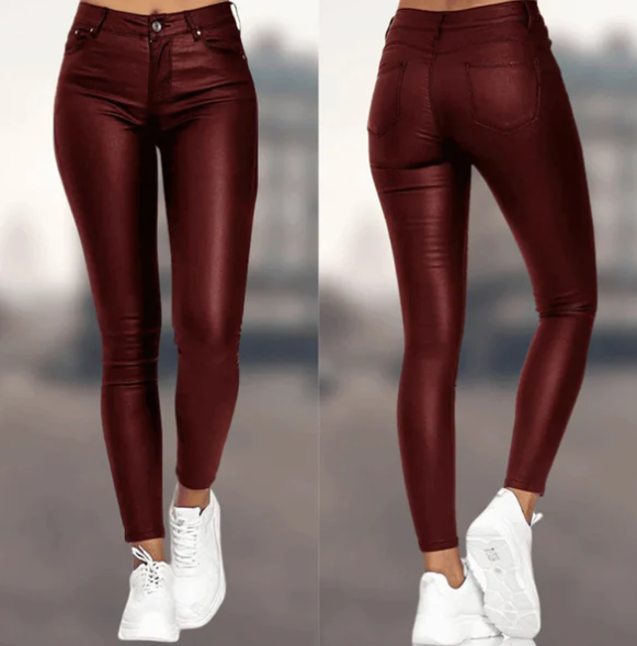 Een vrouw draagt een bordeauxrode, hoog-taille broek van Onyx met een leren uitstraling. De broek heeft een strakke pasvorm en is stijlvol gecombineerd met witte sneakers, waardoor het een elegante en moderne look creëert.