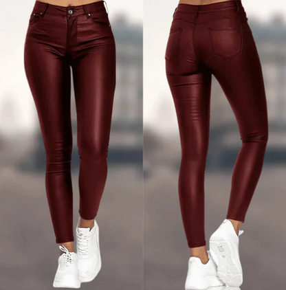 Een vrouw draagt een bordeauxrode, hoog-taille broek van Onyx met een leren uitstraling. De broek heeft een strakke pasvorm en is stijlvol gecombineerd met witte sneakers, waardoor het een elegante en moderne look creëert.