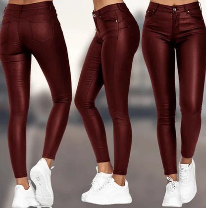 Een vrouw draagt een bordeauxrode, hoog-taille broek van Onyx met een leren uitstraling. De broek heeft een strakke pasvorm en is perfect gestyled met witte sneakers, wat zorgt voor een moderne en elegante uitstraling