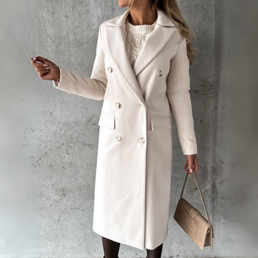 Ulara Winterjas in stijlvol gebroken wit. Elegante lange damesjas met dubbele rij knopen, brede revers en een getailleerd design. Perfect voor een verfijnde en functionele winterlook.