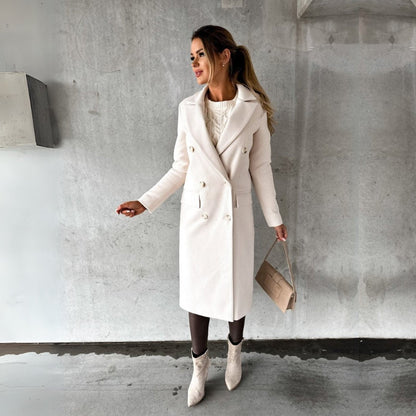 Ulara Winterjas - Een elegante lange dames winterjas in gebroken wit met een stijlvolle pasvorm, dubbele rij knopen en brede revers. Gecombineerd met een chique handtas en enkellaarsjes voor een complete, verfijnde look.