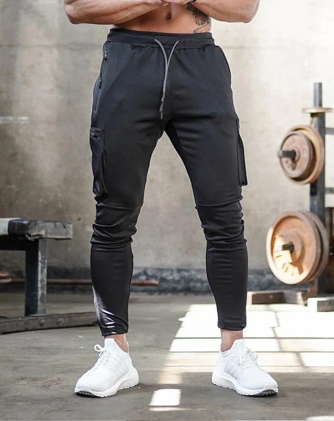 Afbeelding van de Umiro cargo jogger in het zwart. Deze stijlvolle en comfortabele jogger heeft een slim-fit pasvorm en is voorzien van praktische cargozakken aan beide zijden. De elastische tailleband met trekkoord zorgt voor een perfecte en verstelbare pasvorm. Het zachte, flexibele materiaal biedt ultiem draagcomfort, ideaal voor sportieve activiteiten of casual outfits.