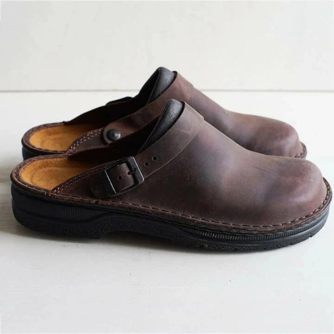 Afbeelding van de Urbano loafers in een stijlvolle donkerbruine leren uitvoering. Deze comfortabele instappers hebben een open hielontwerp en een verstelbare gesp voor een perfecte pasvorm. De stevige zool biedt uitstekende grip en ondersteuning, terwijl het zachte voetbed zorgt voor langdurig draagcomfort. Ideaal voor zowel binnen als buiten gebruik, met een klassieke en tijdloze uitstraling.