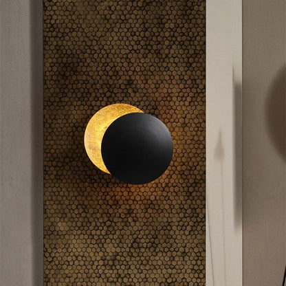 Wandlamp met zonsverduistering - Een stijlvolle en sfeervolle wandlamp met een uniek ontwerp dat een zonsverduistering nabootst. De zwarte ronde schijf blokkeert deels het warme gouden licht, wat een rustgevende en elegante uitstraling creëert. Perfect voor het toevoegen van een artistiek en modern element aan elke kamer